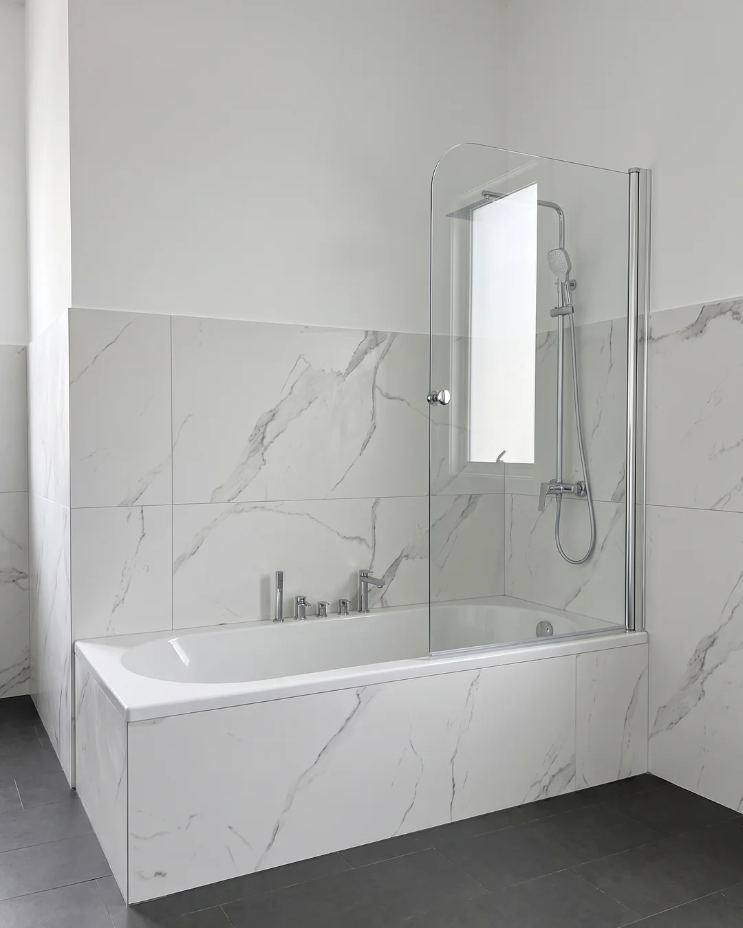 Mampara abatible para bañera con cristal transparente sobre alicatado de mármol blanco