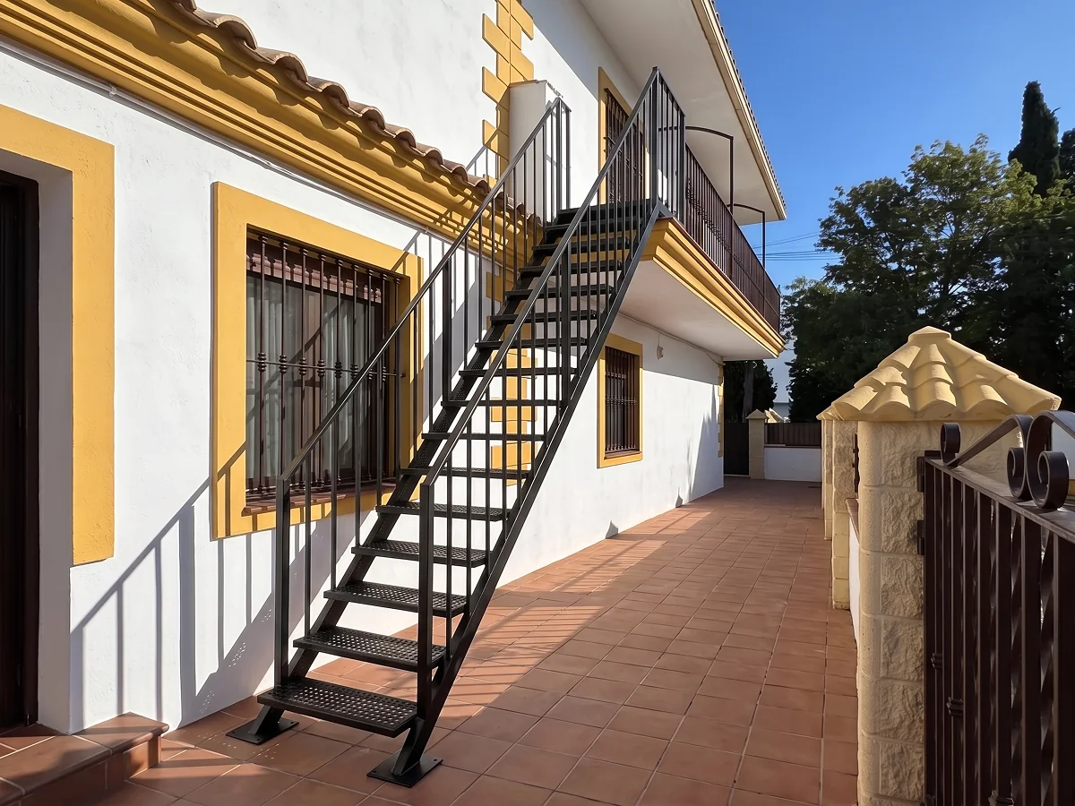 Escalera recta exterior de hierro con barandilla y peldaños antideslizantes en Sevilla