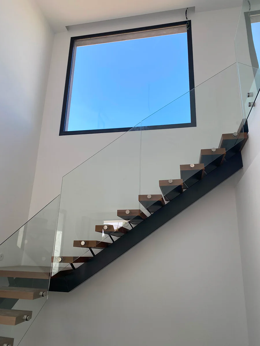 Escalera de viga central de acero bajo ventanal a doble altura · Madera no incluida