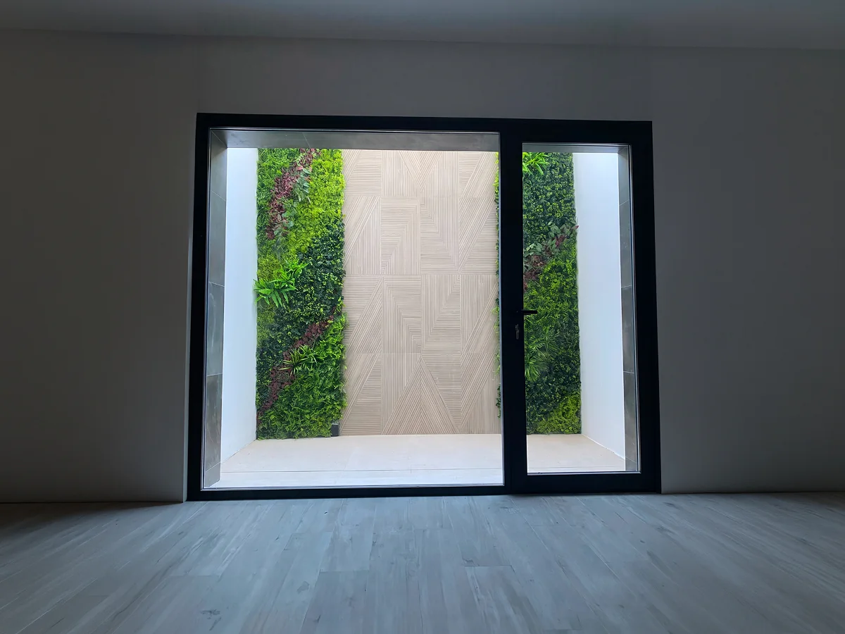 Puerta corredera de vidrio con perfilería de aluminio negro abierta a jardín vertical en Sevilla