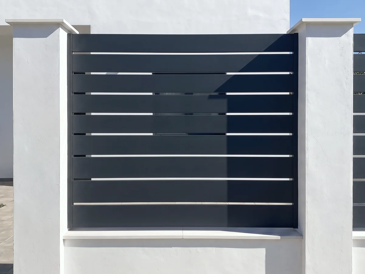Valla de jardín con panel de lamas horizontales de hierro antracita entre pilares en Sevilla